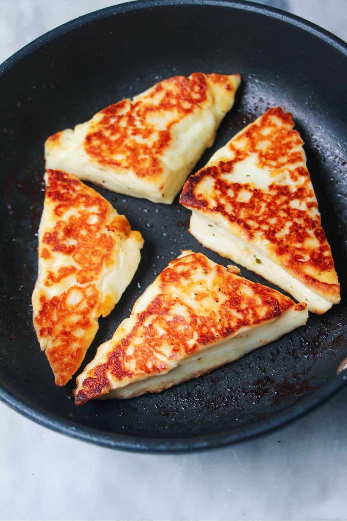 4 wedges of golden pan fried halloumi in a small black pan.
