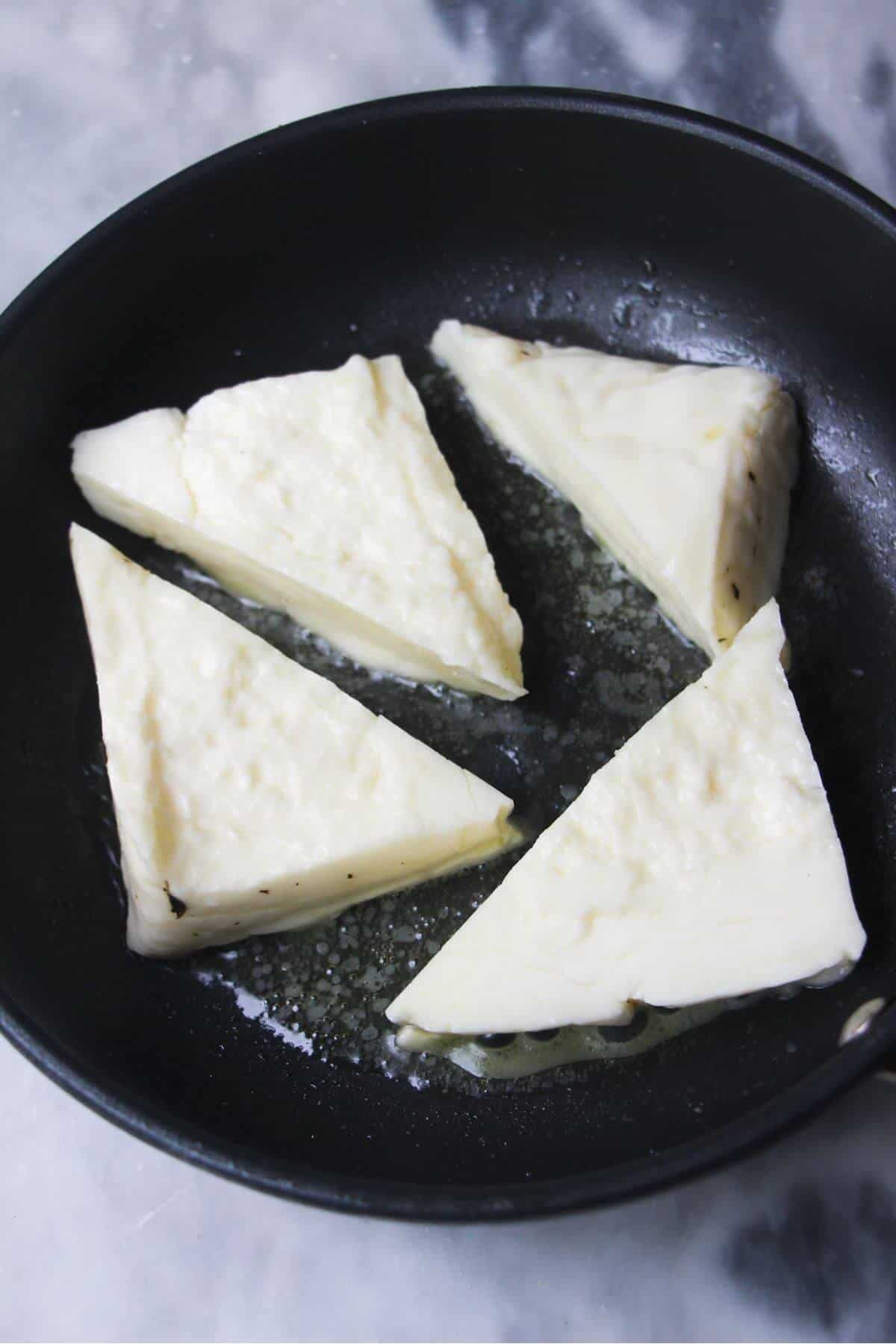 4 wedges of halloumi in a small black pan.
