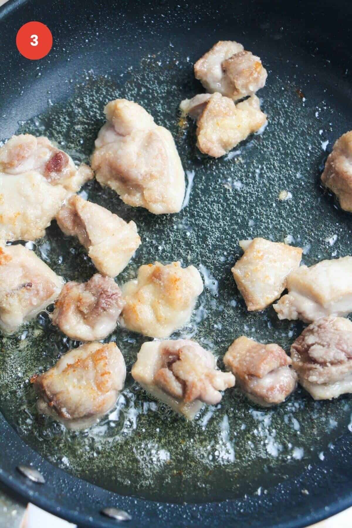 Chicken pieces cooking in pan.