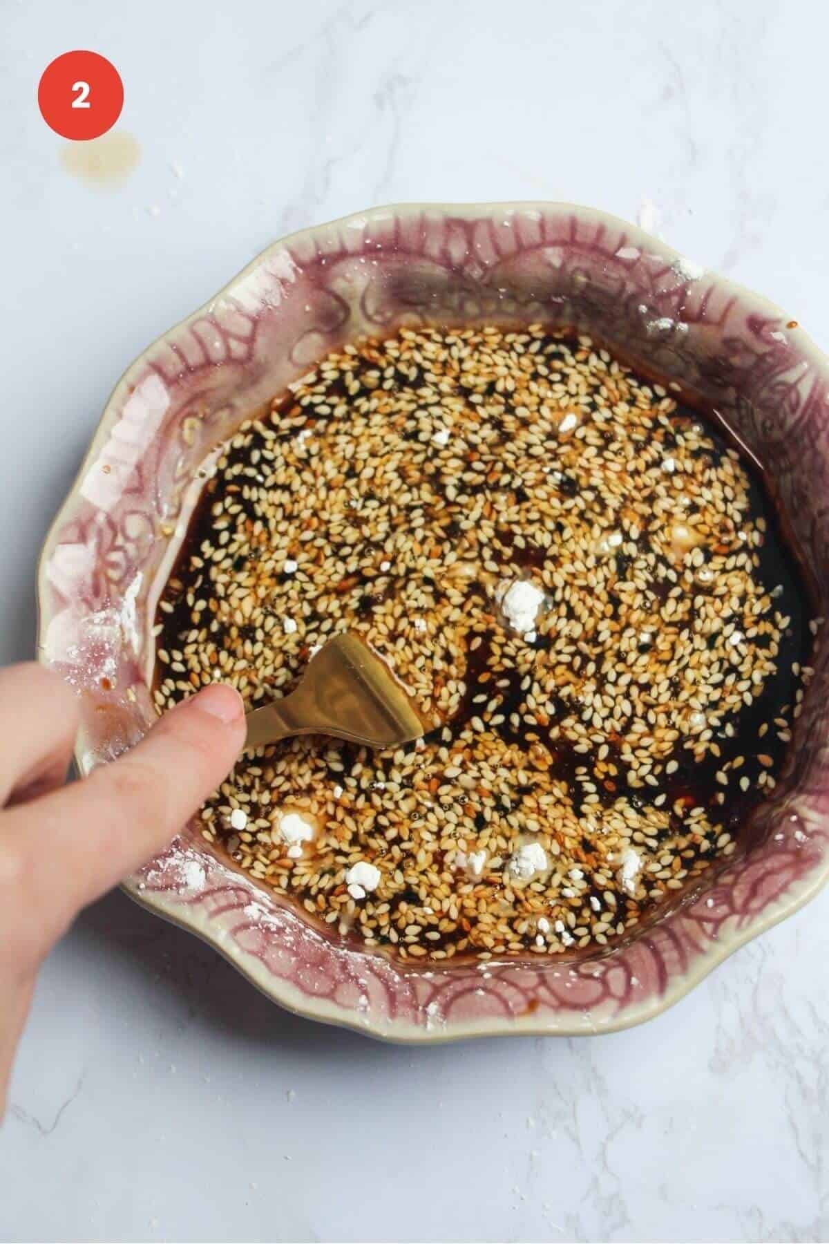 Fork mixing honey sesame sauce in bowl.