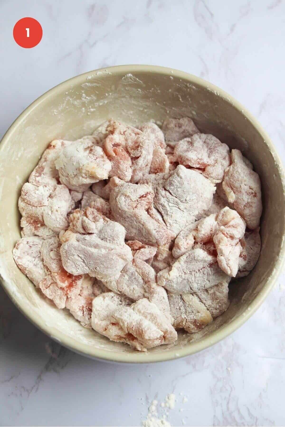 Chicken pieces tossed in cornstarch in a bowl.
