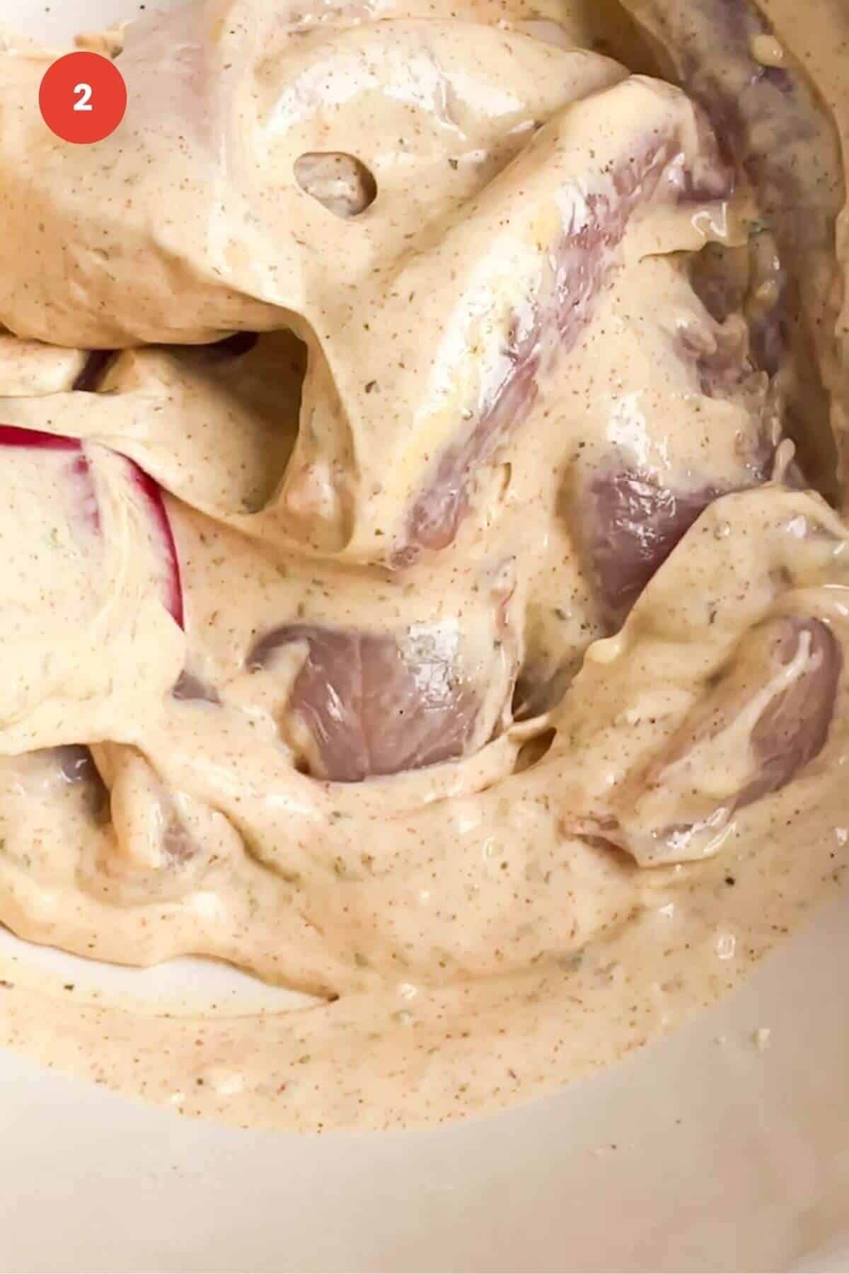Chicken tenders mixed with yogurt marinade in bowl.