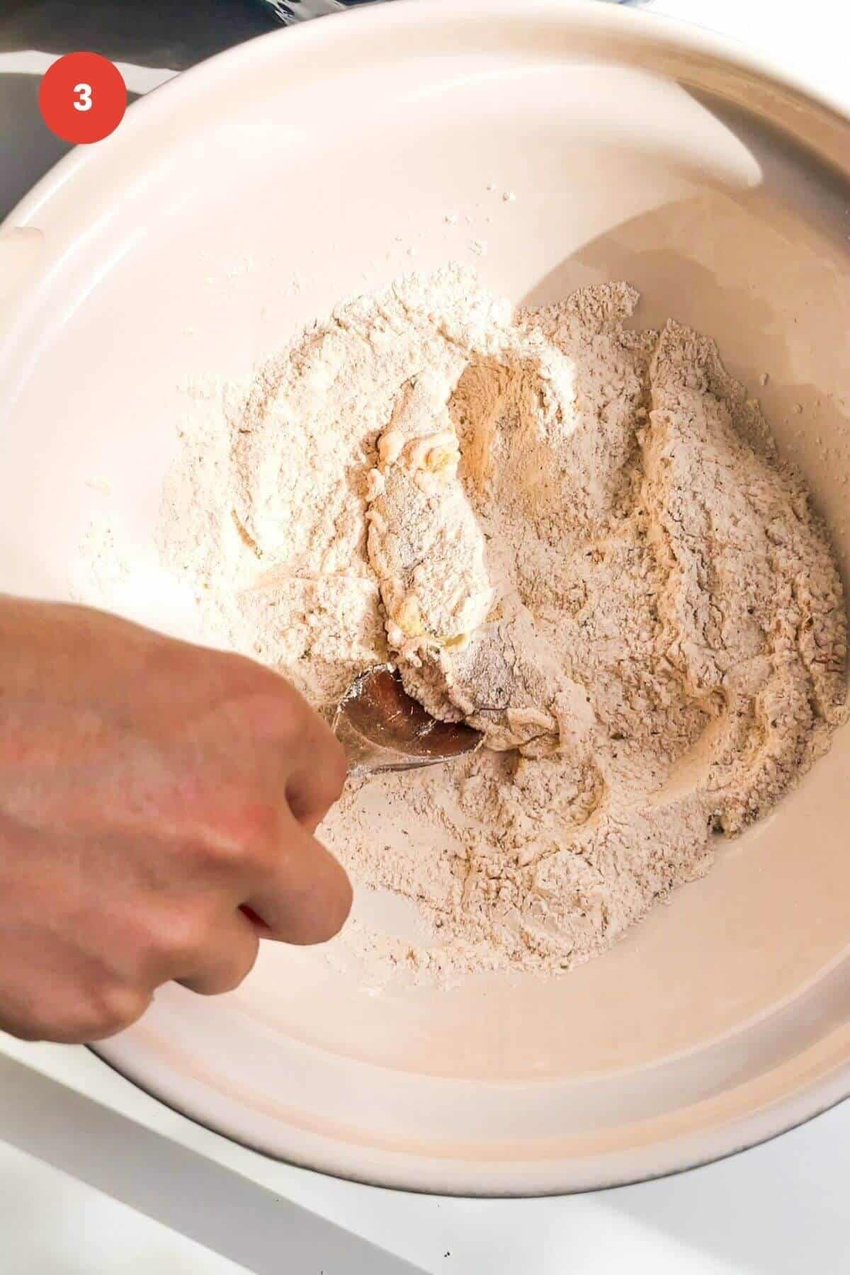 Hand holding spoon, mixing flour and spices in a bowl.