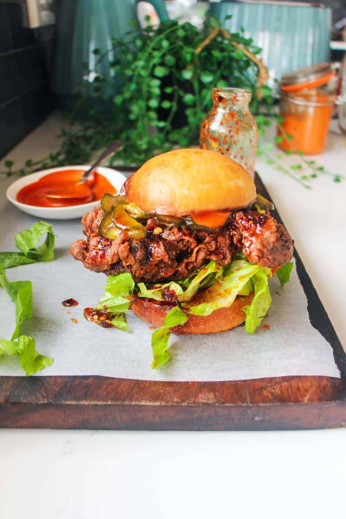 Hot honey fried chicken sanwich on a dark wooden board with small bowl of gochujang aioli in the background.