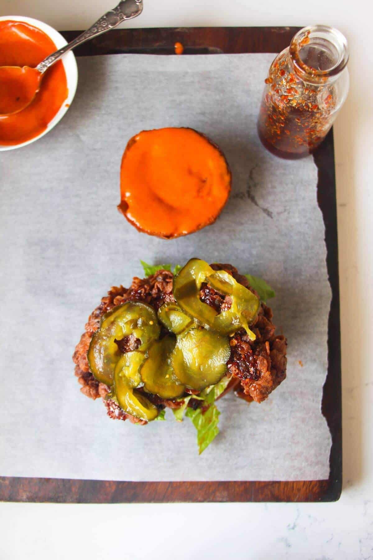 Sliced pickles on top of piece of fried chicken on a burger bun.