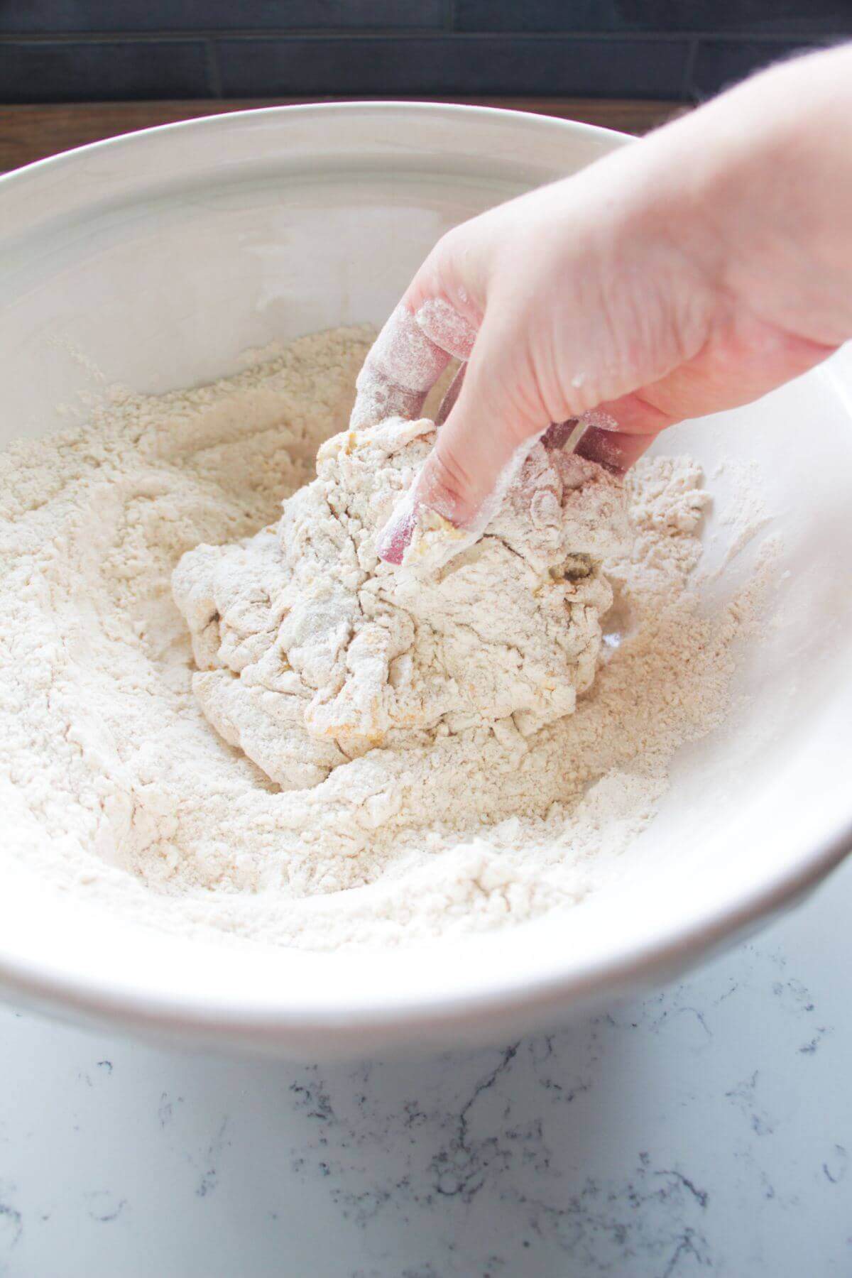 Hand dredging chicken thigh in flour and spices.