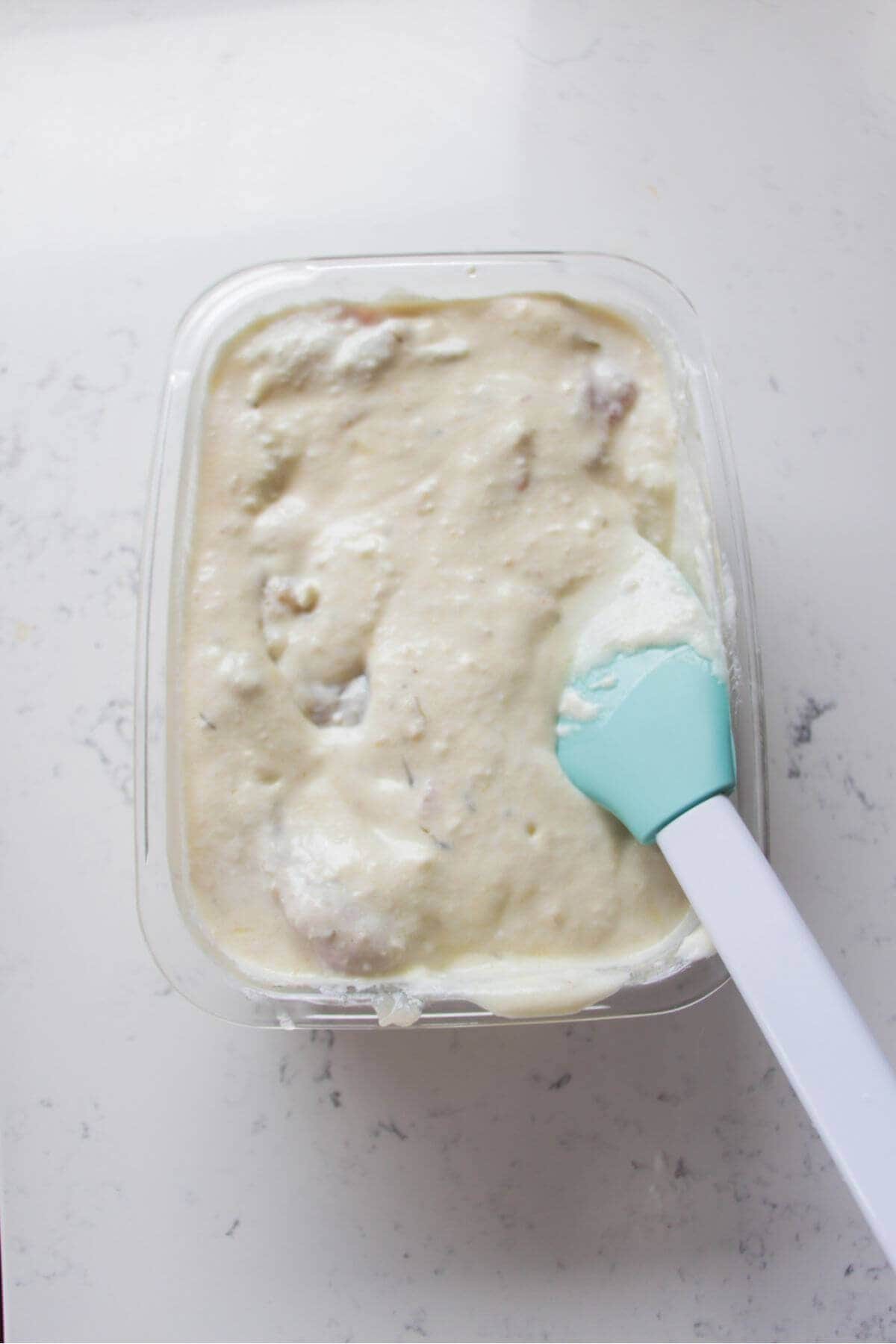 Chicken thighs in yogurt marinade in a glass container.