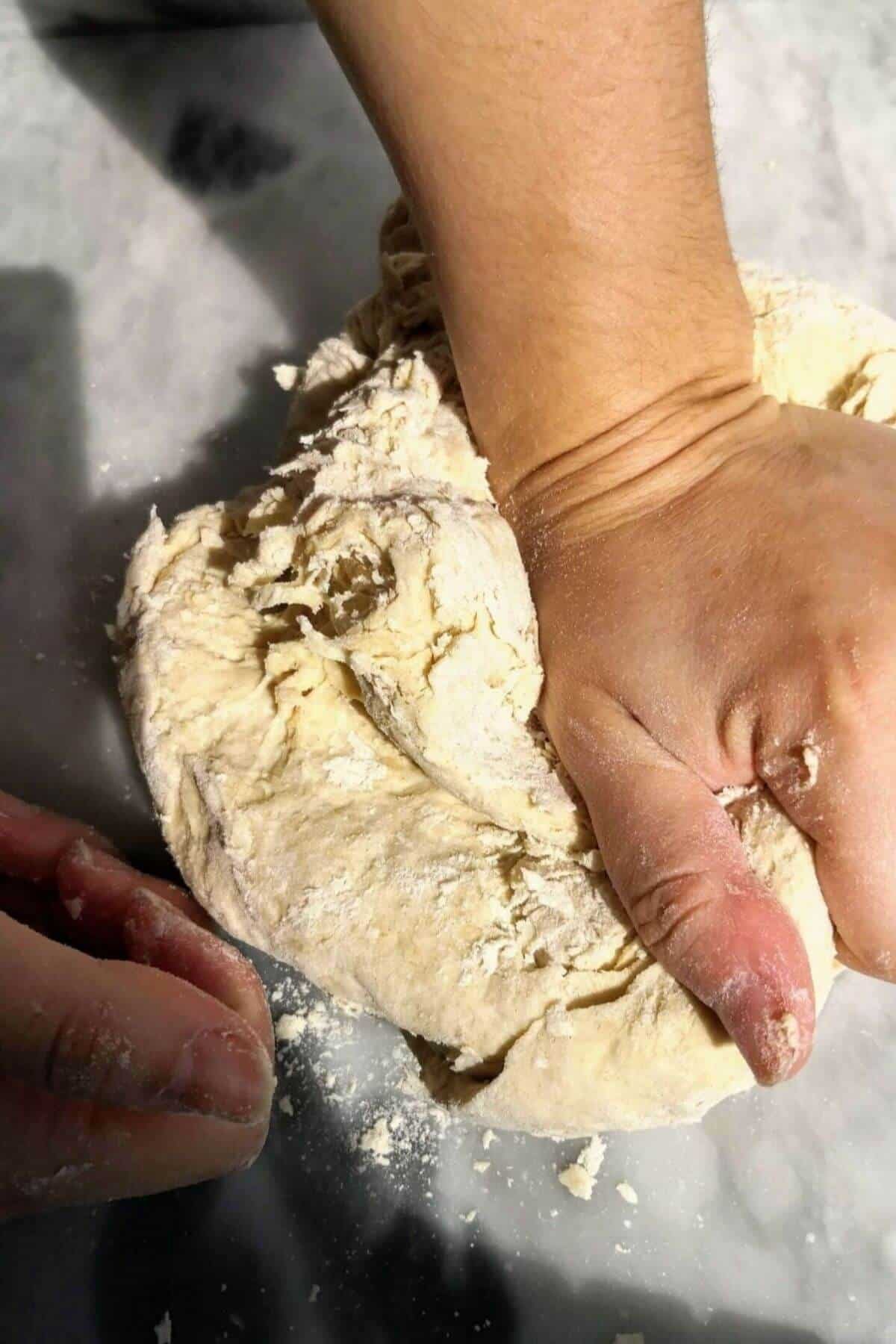 Hand kneading dough on bench.