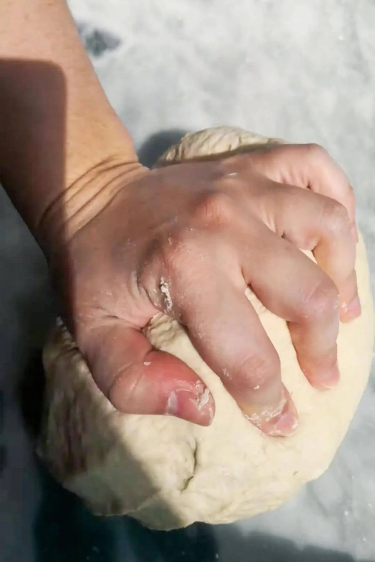 Hand kneading dough on bench.