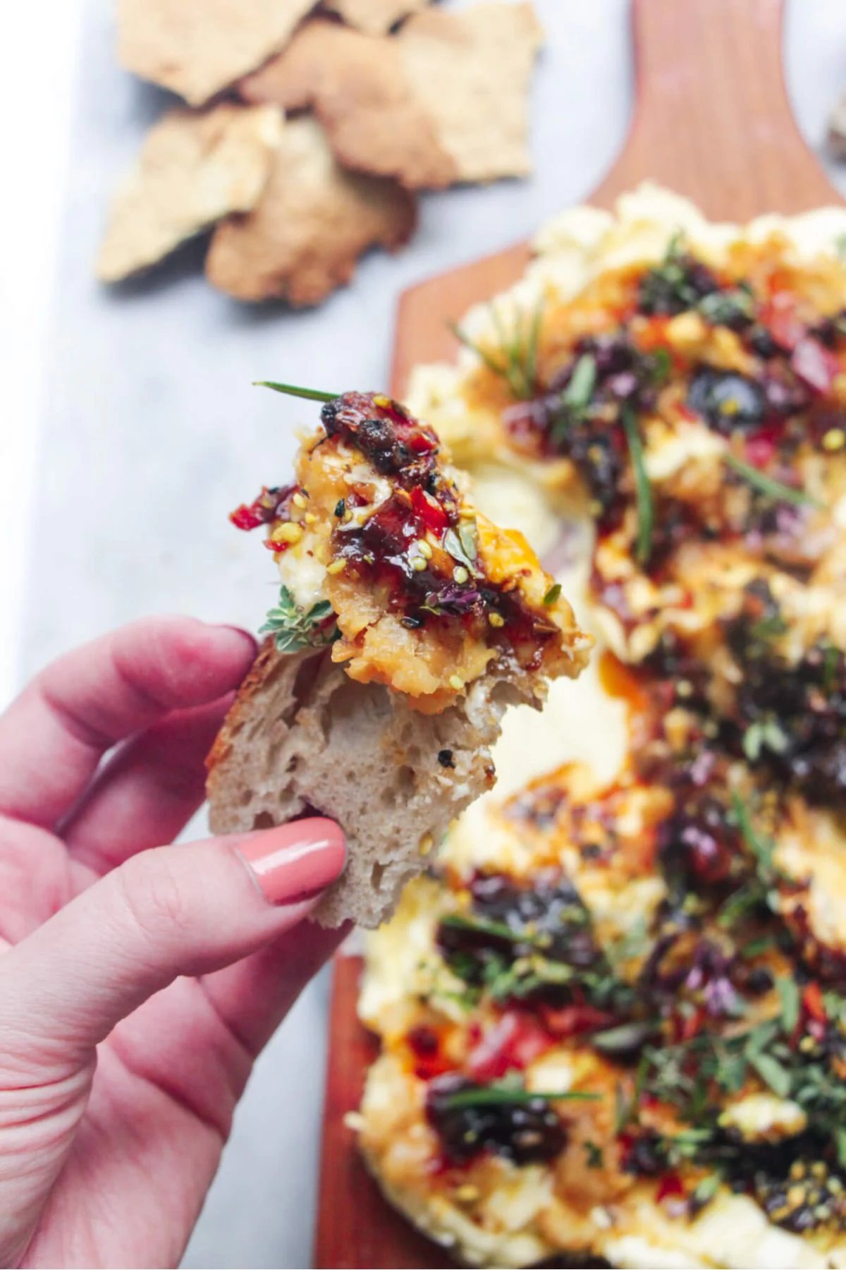 Hand holding up a piece of bread with butter and toppings on it.