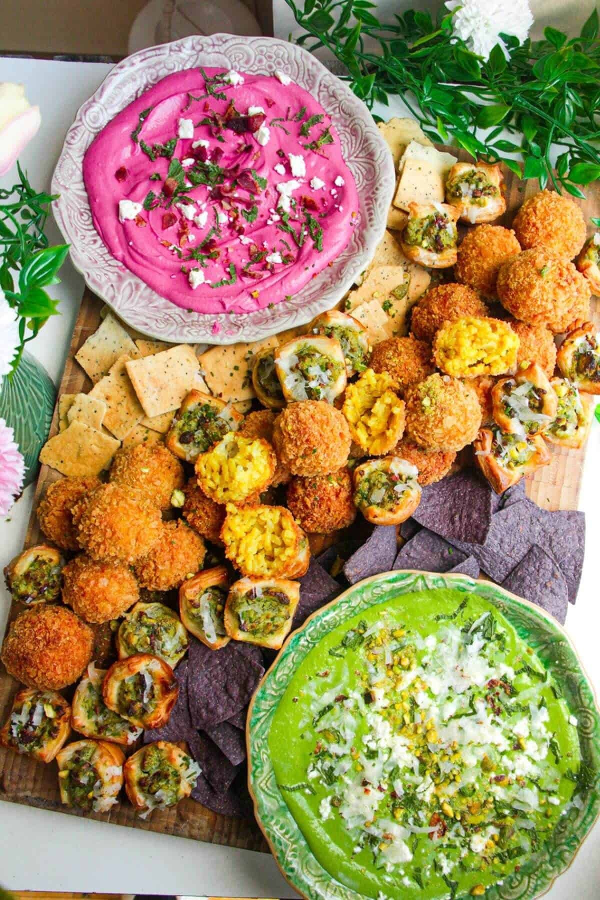 Dips, arancini and puff pastry bites on a wooden board.