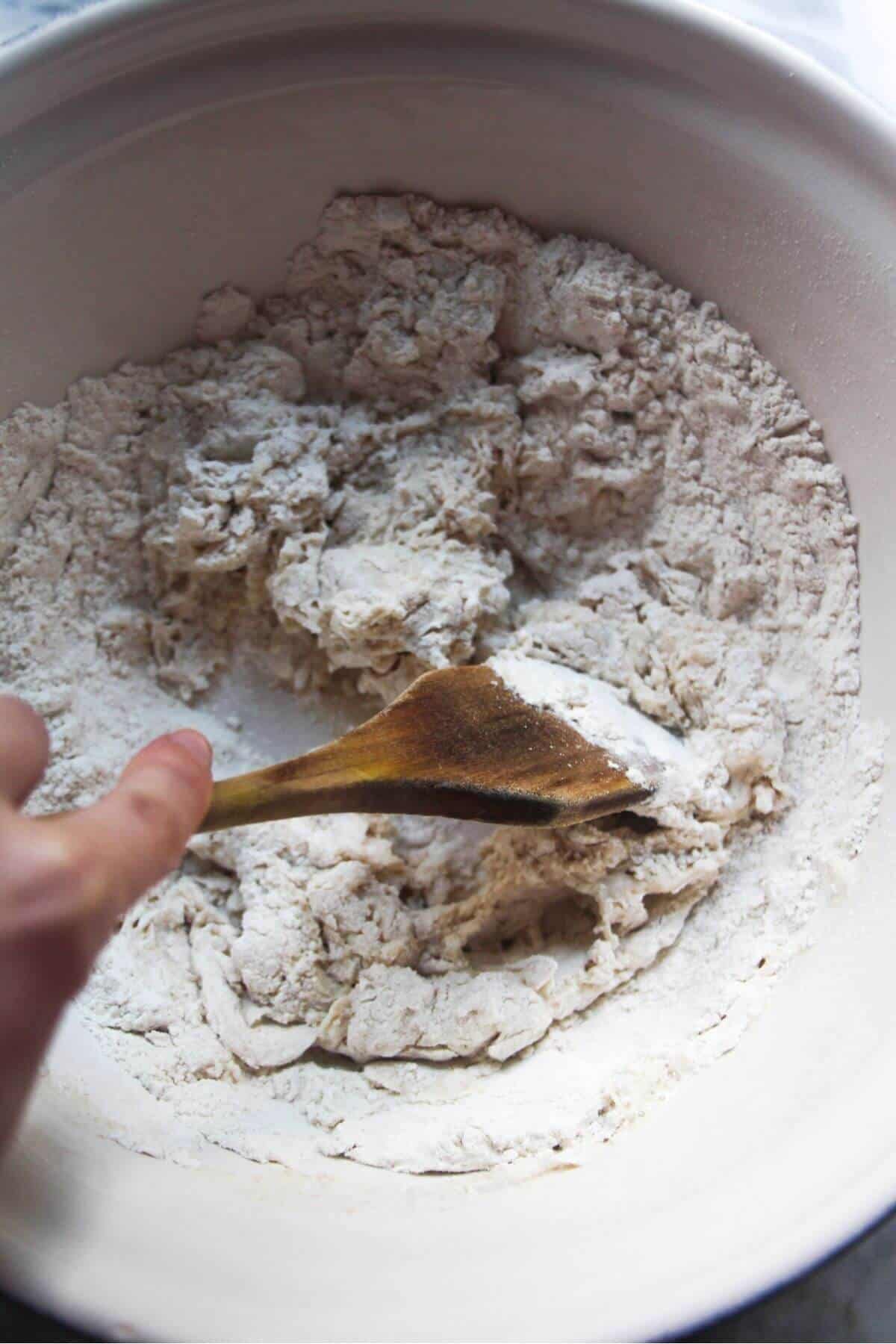 Bao ingredients in a large silver mixing bowl, with water being poured in.
