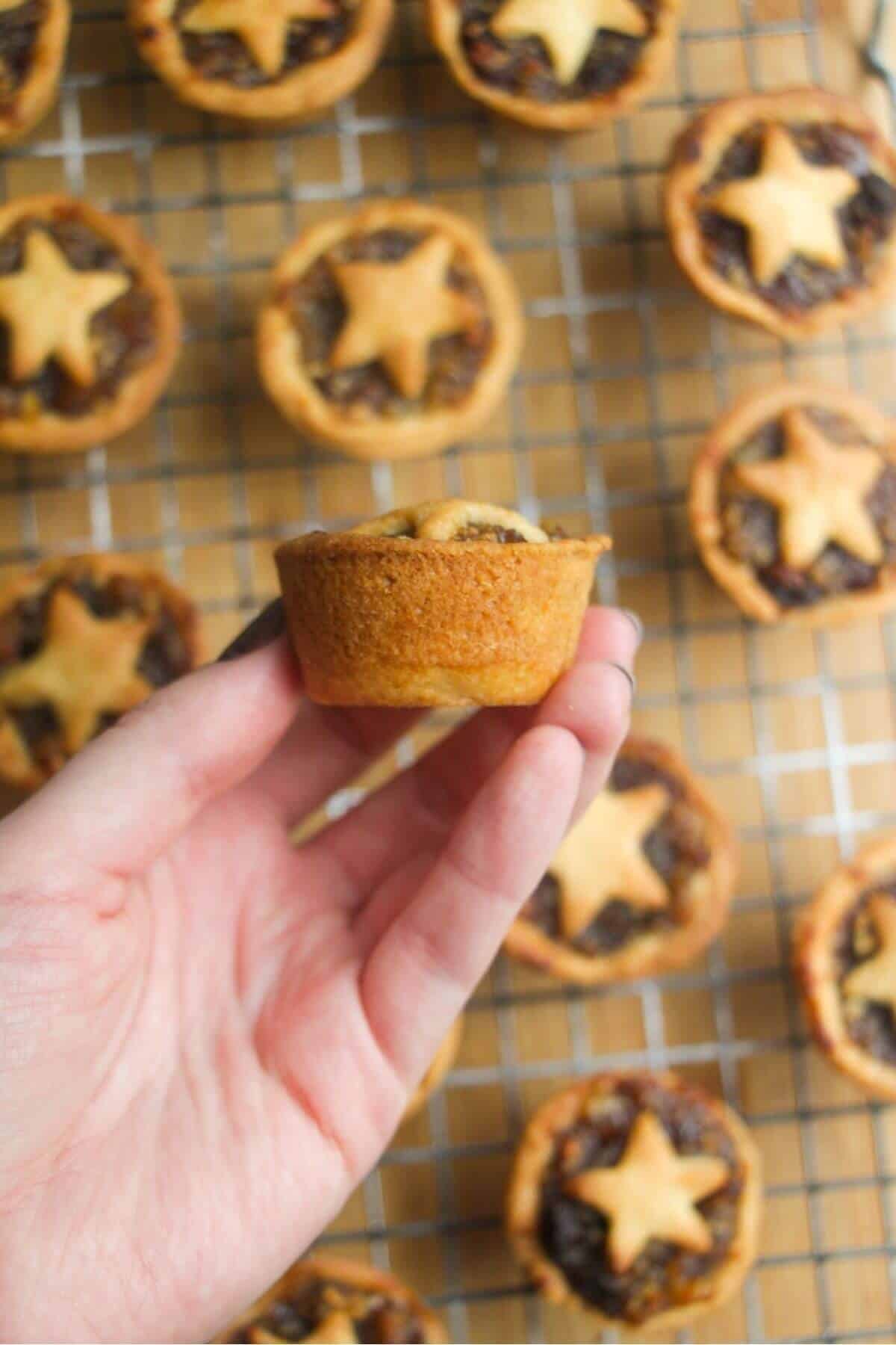 A hand holding up a fruit mince pie, showing the side of the pie.