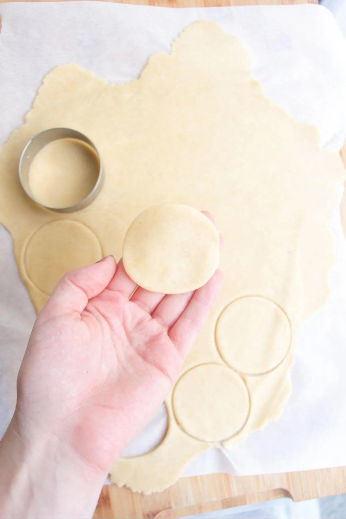A hand holding up small pastry circle with more pastry in the background.