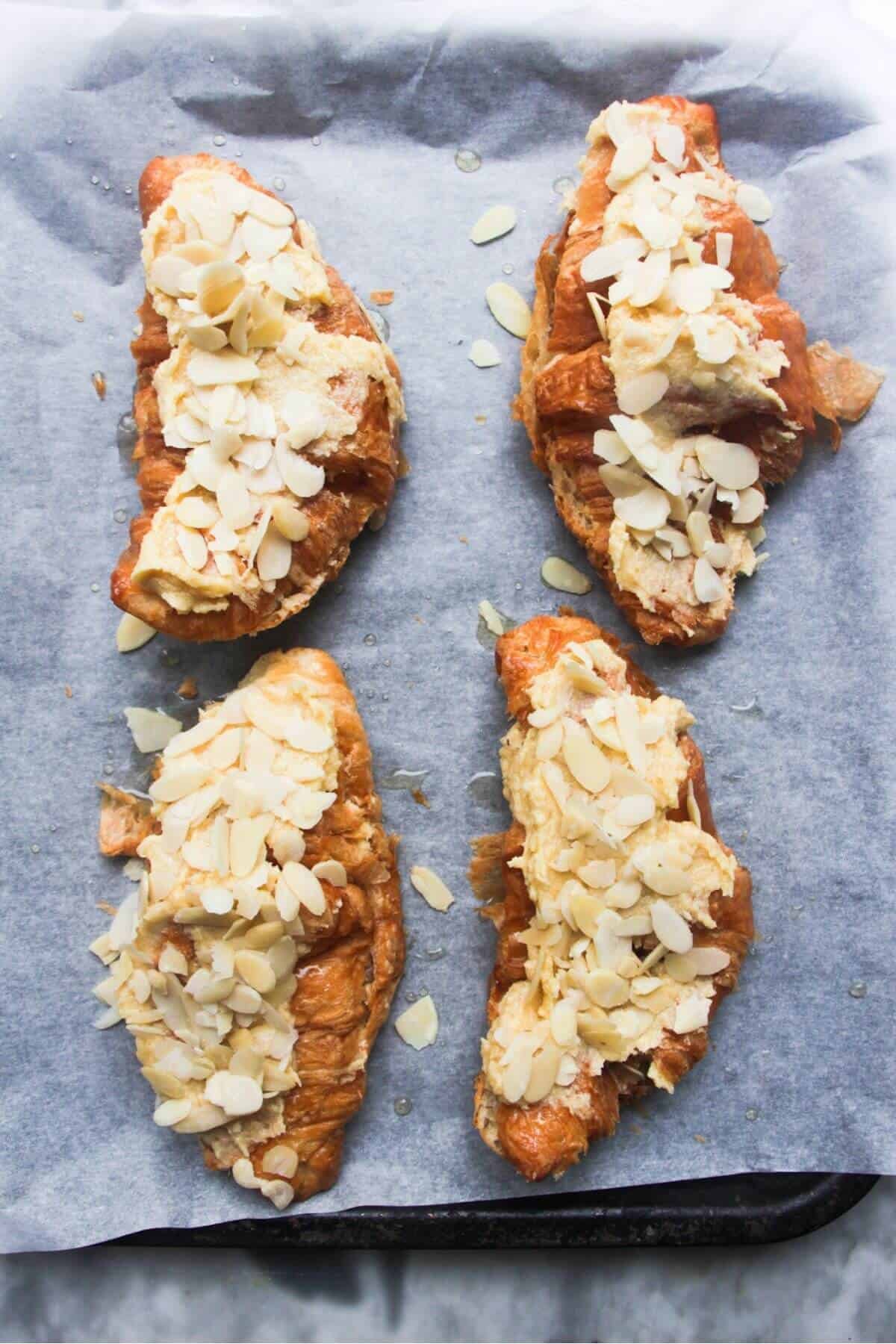 Four almond croissants on a lined oven tray ready to be baked.