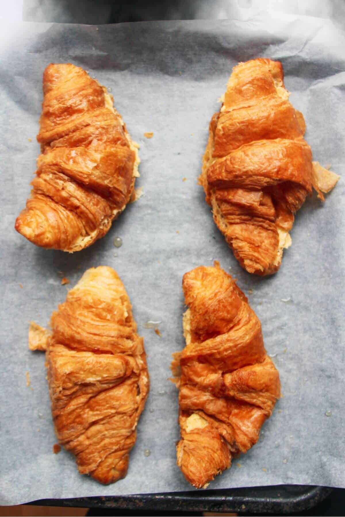 Four croissants on a baking tray ready to be topped with almond frangipane.