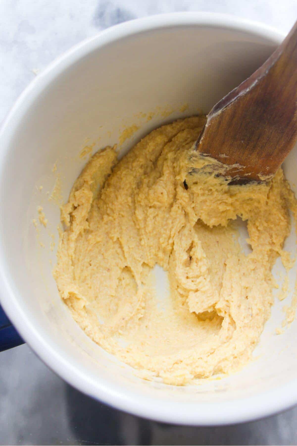 A large wooden spatula mixing almond frangipane in a white bowl.