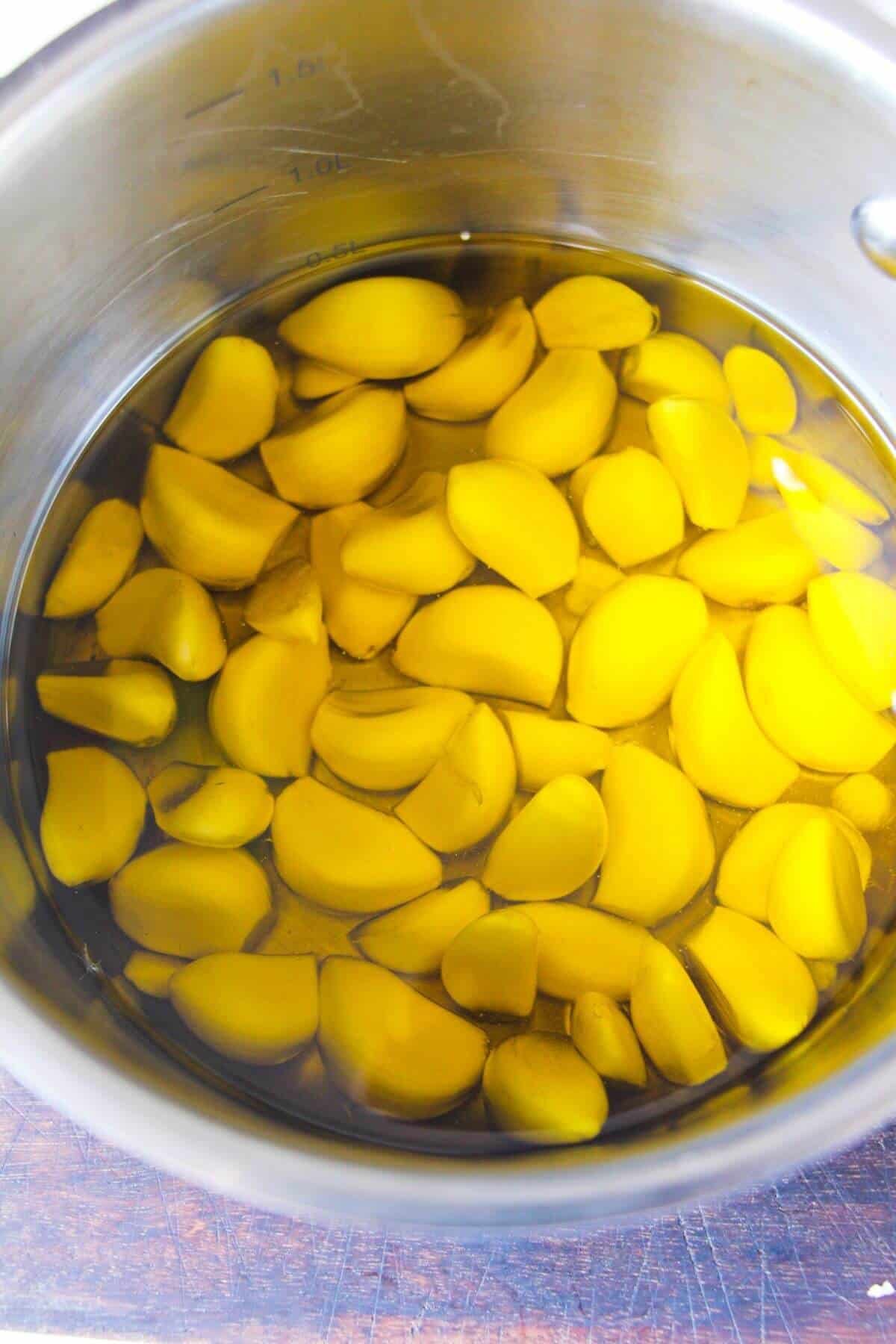 Garlic cloves in olive oil in a small silver pot.