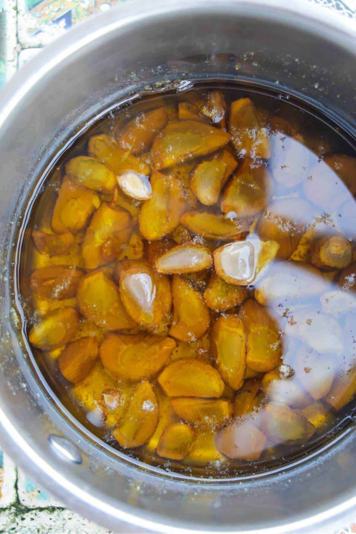 Garlic cloves in olive oil in a small silver pot.