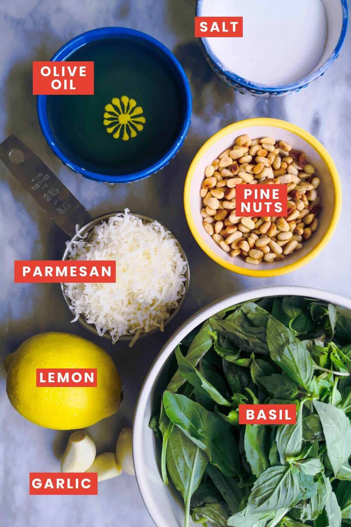 Ingredients for basil pesto laid out on a grey marble background and labelled.