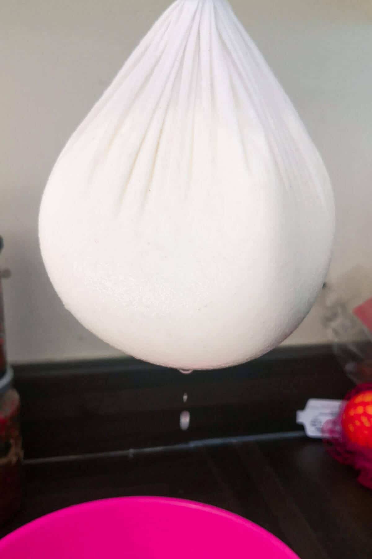 Yogurt in cheesecloth hanging over a pink bowl.