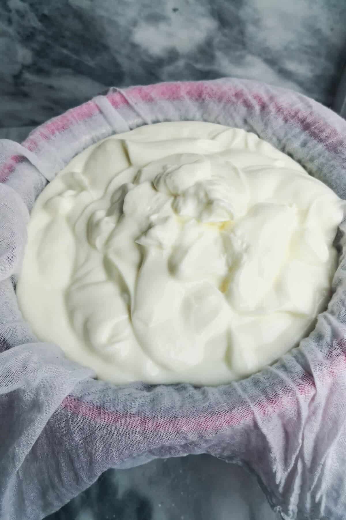 Yogurt in cheesecloth set over a sieve and pink bowl.