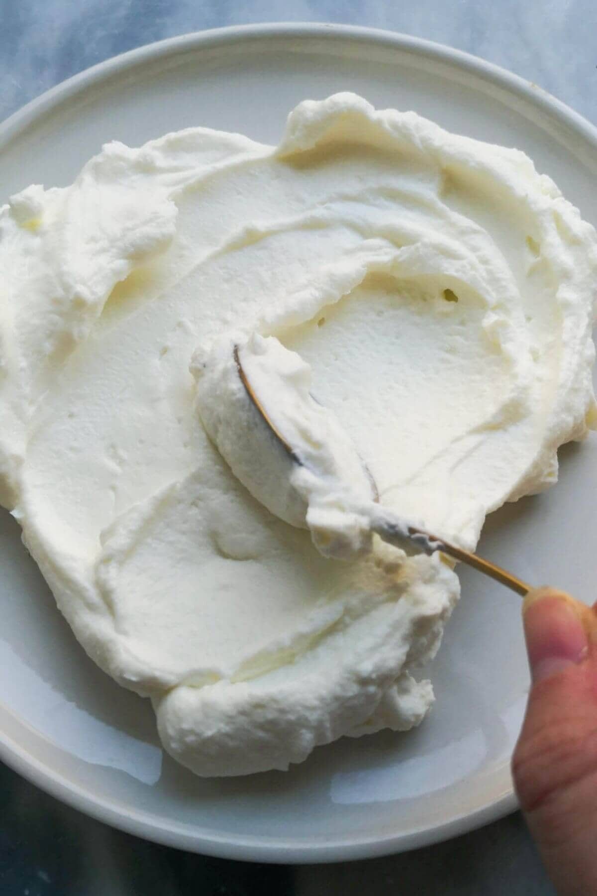 Gold spoon smoothing labneh onto a small white plate.