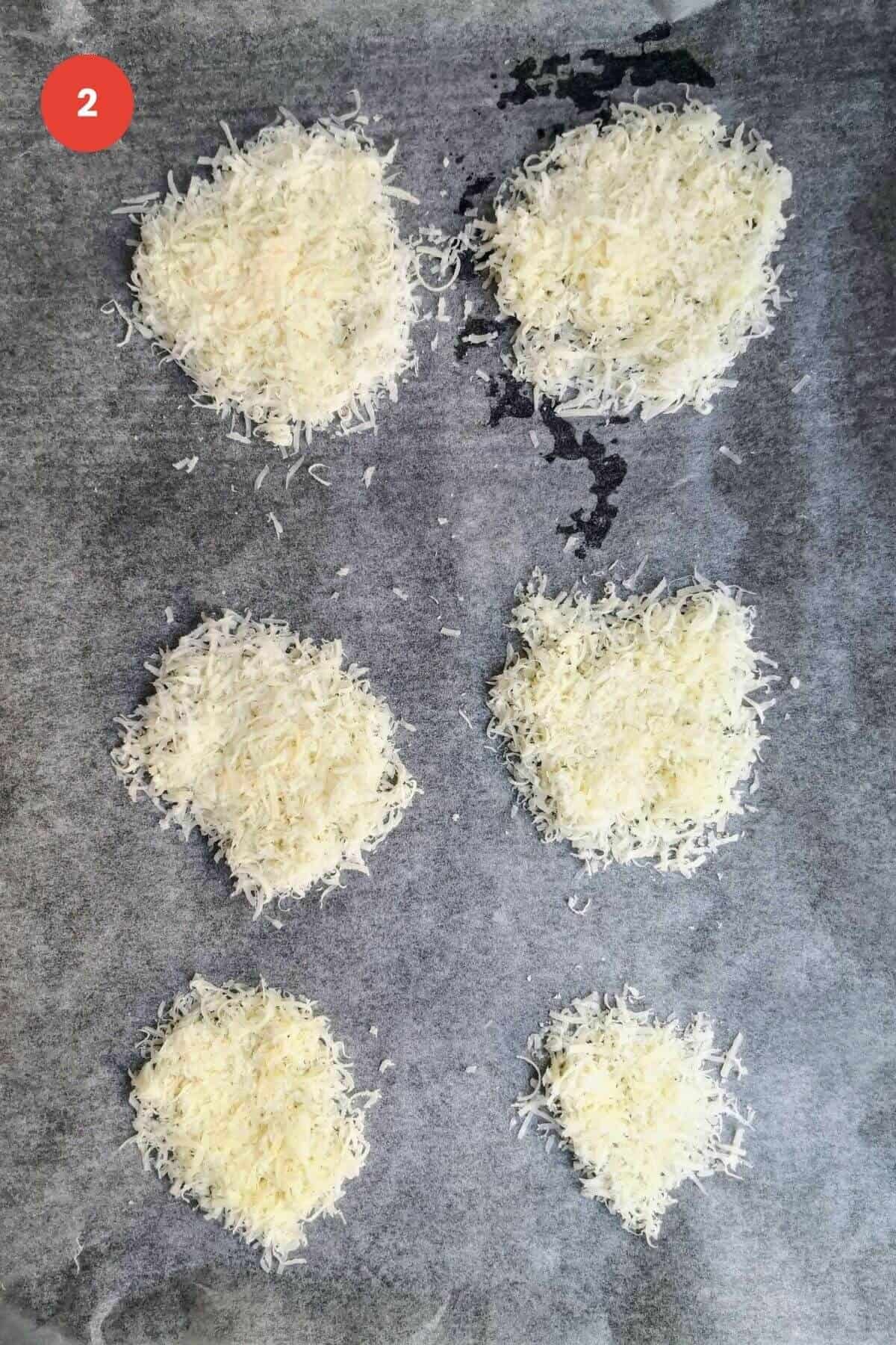 Six piles of grated parmesan cheese on a baking pan.