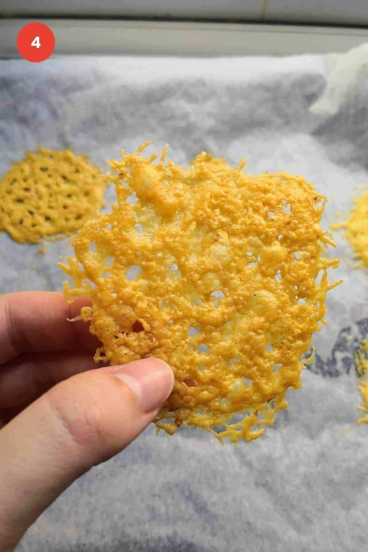 Hand holding a parmesan crisp with more in the background.