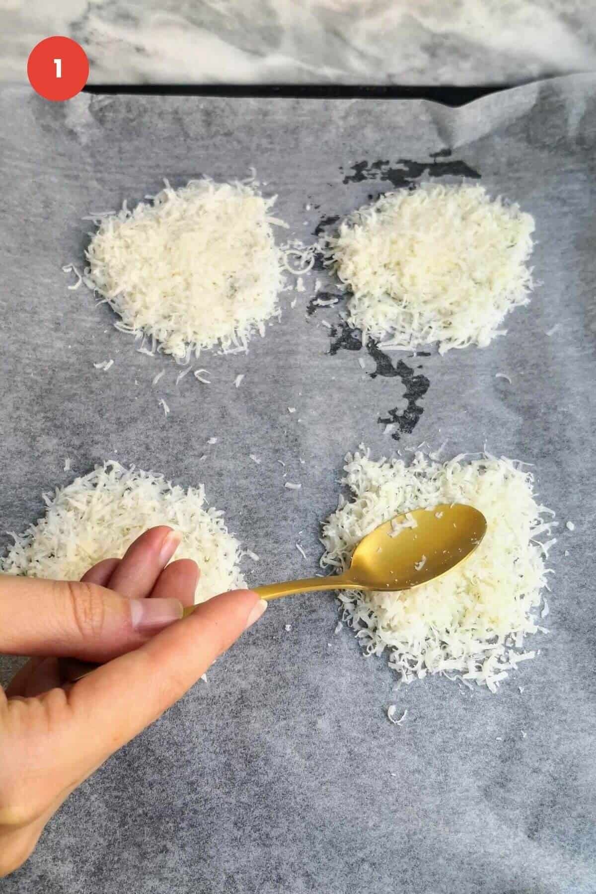 Spoon pressing down on parmesan cheese circles on baking pan.