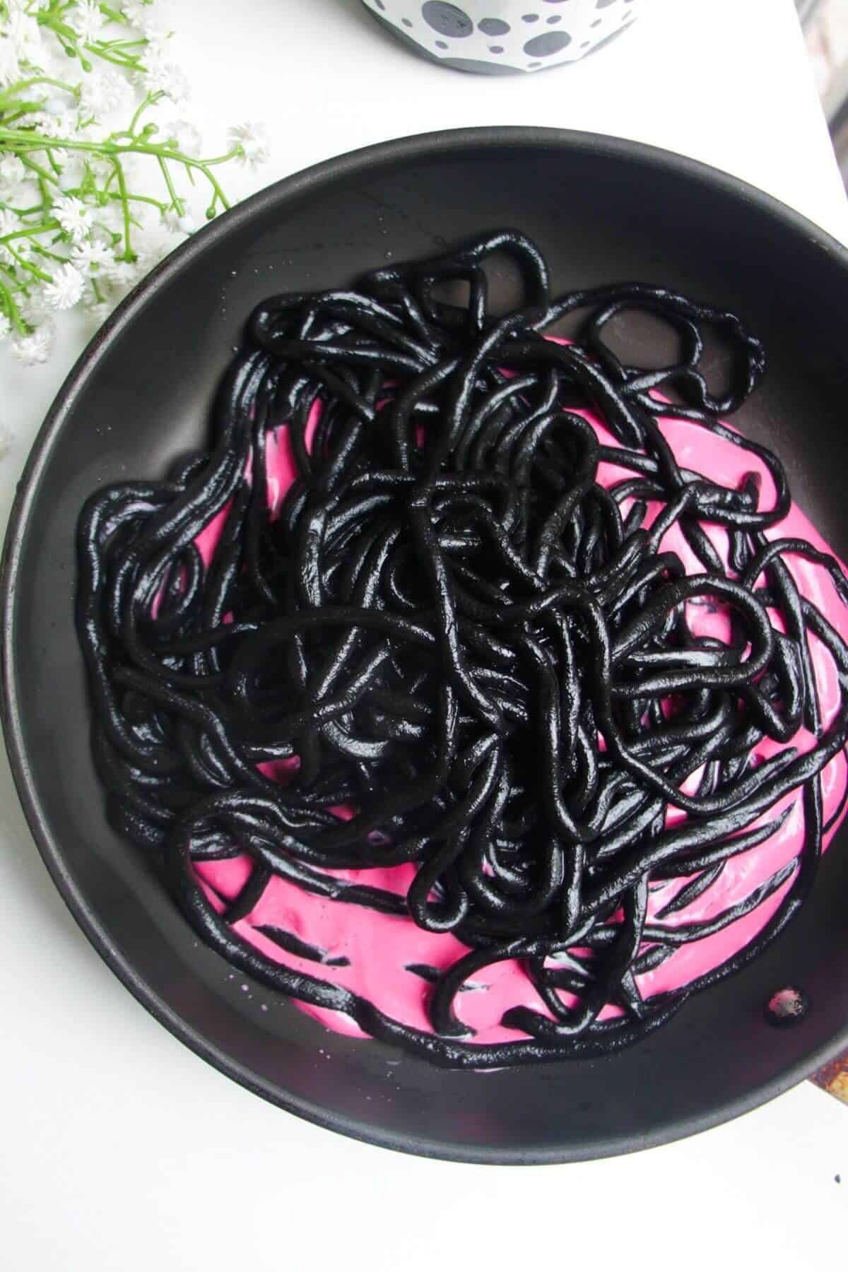 Squid ink pici in pink beet pasta sauce in a pan.