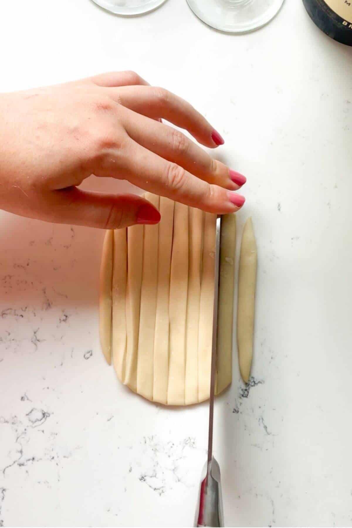 Knife slicing through pici dough on the kitchen counter.