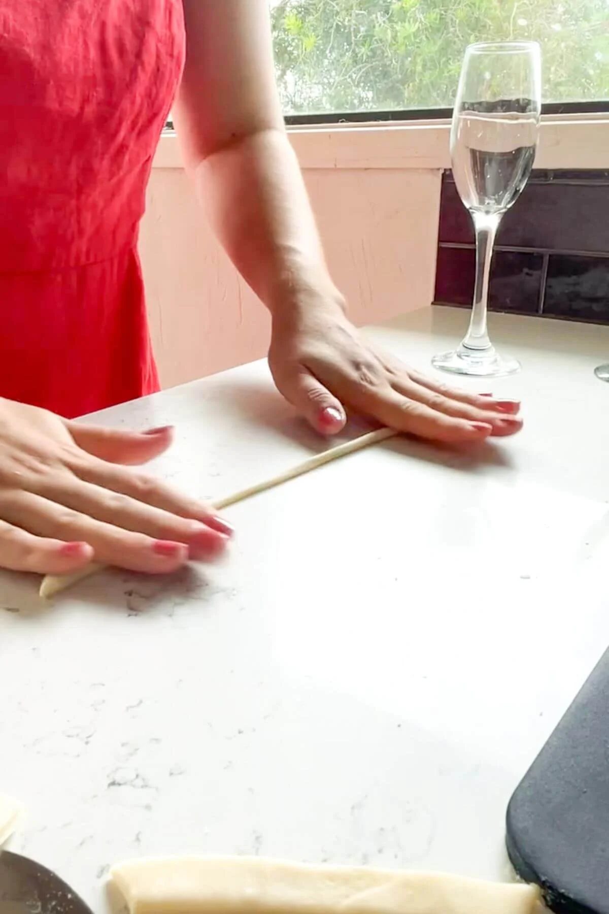 Hands rolling out a strand of pici pasta on the kitchen counter.