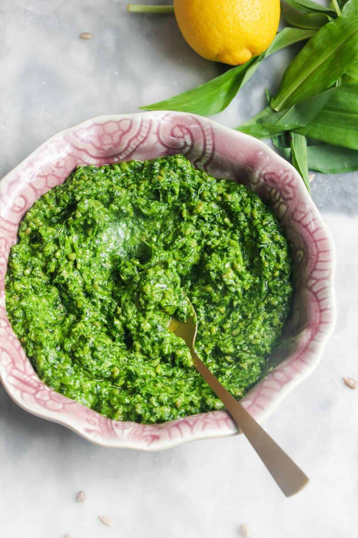 Bright green wild garlic pesto in a small pink bowl on a grey marble background.
