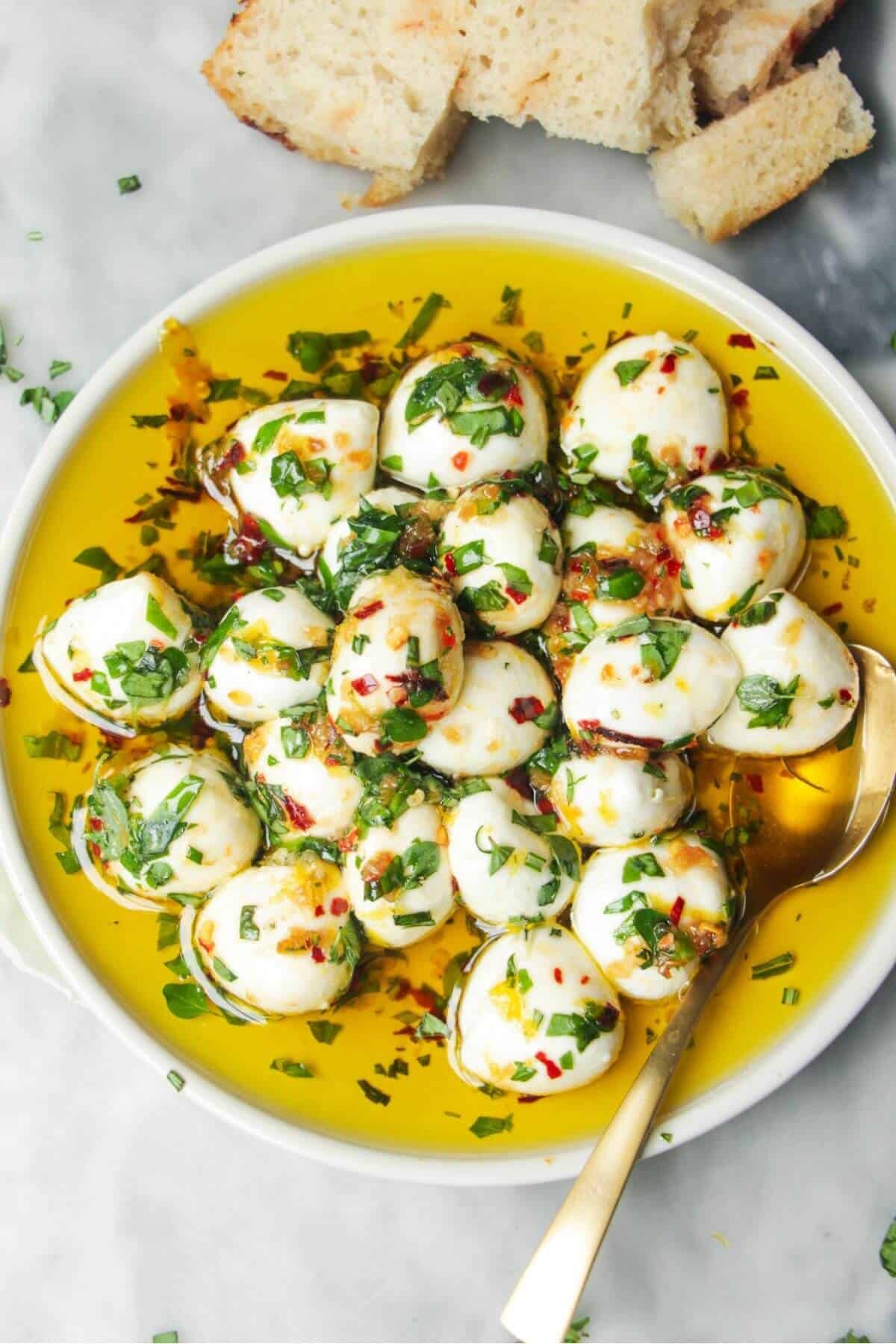 Marinated mini mozzarella balls in a small white plate with a gold spoon.