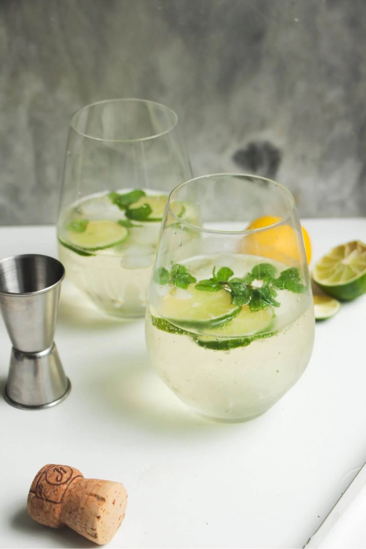 2 glasses of Hugo spritz with lime slices and mint leaves inside.