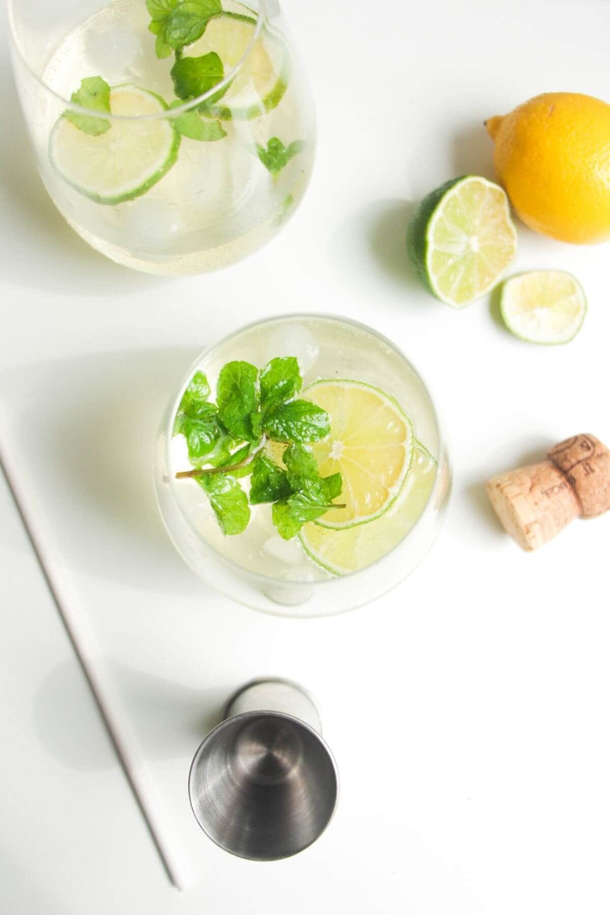 2 glasses of Hugo spritz with lime slices and mint leaves inside.