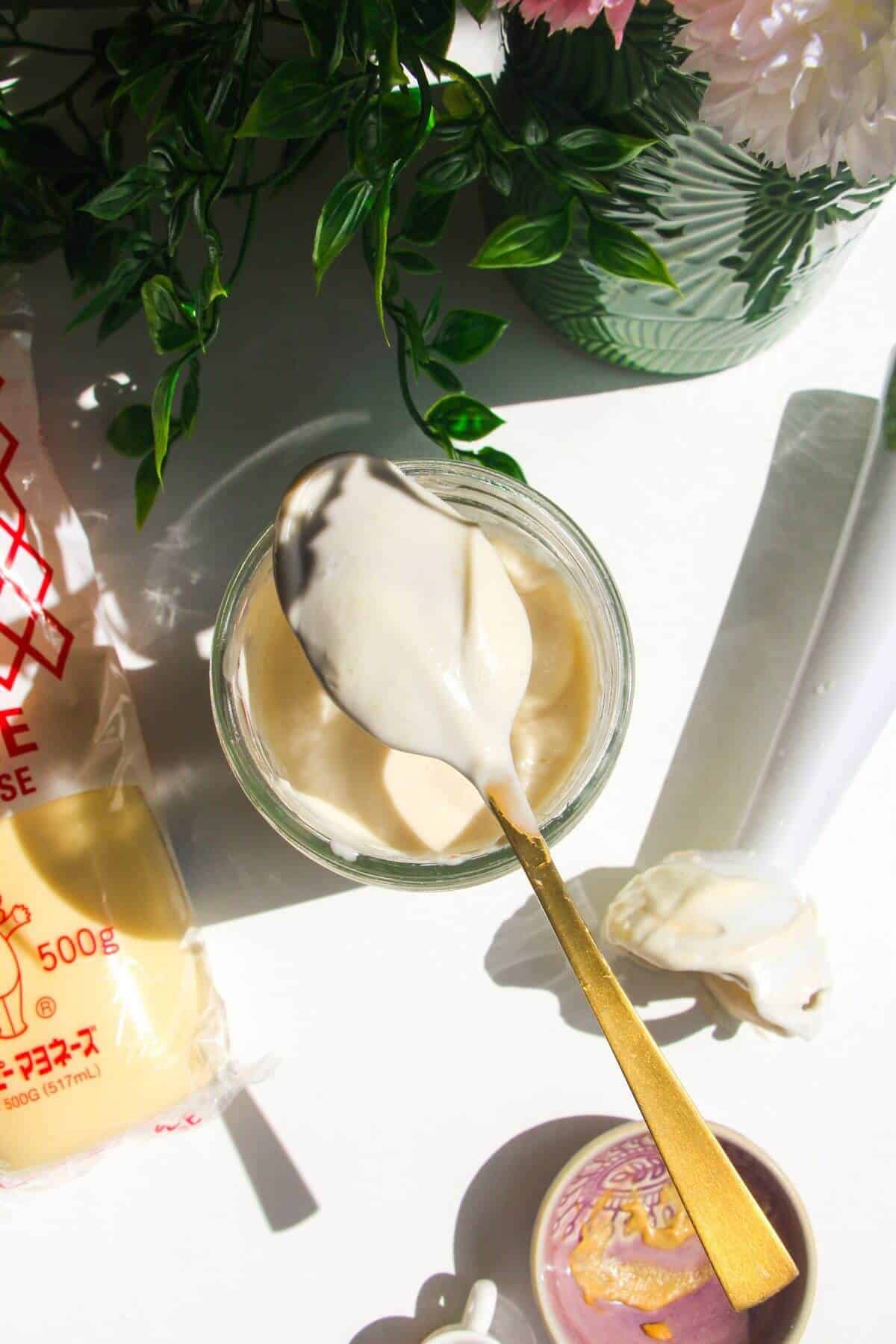 Kewpie mayo in a glass jar with a spoon on top covered in mayo.