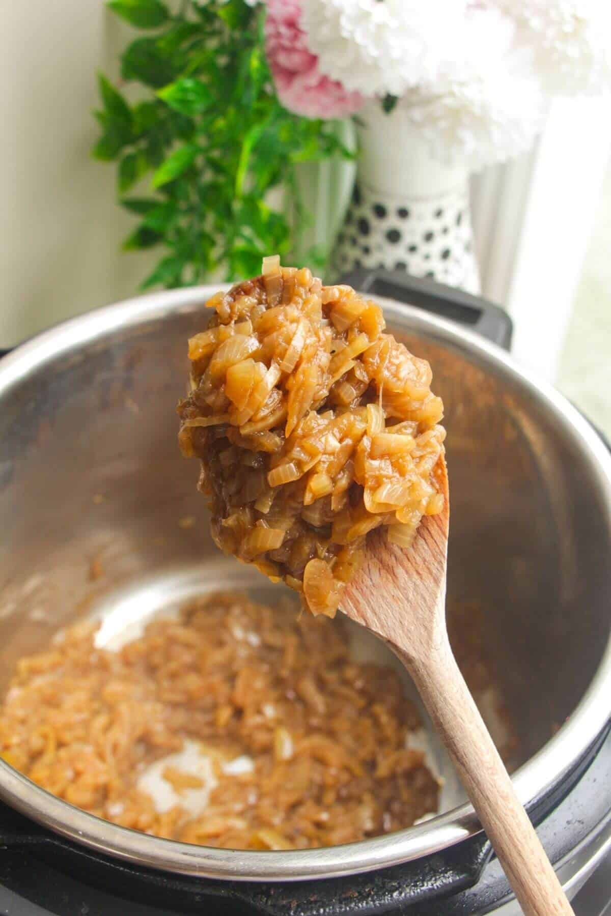 Wooden spoon with caramelized onions, with Instant Pot in the background.