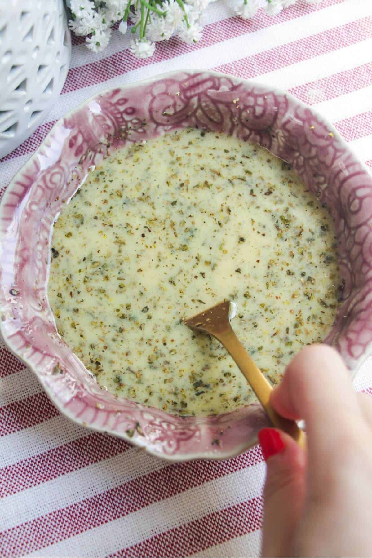 Hand holding fork mixing Italian dressing in a pink bowl.