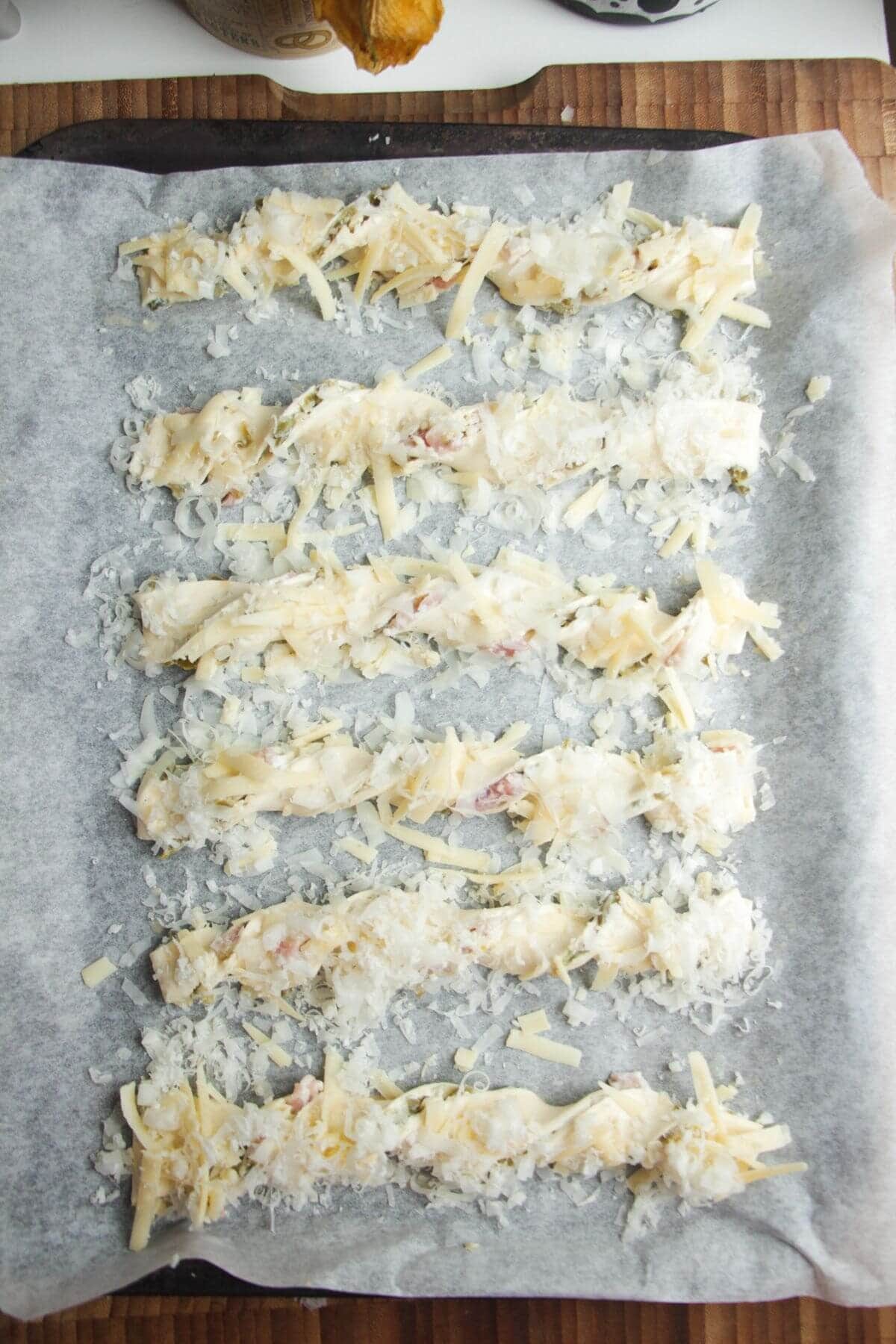 Twisted and cheese topped jalapeno popper straws on a lined oven tray.