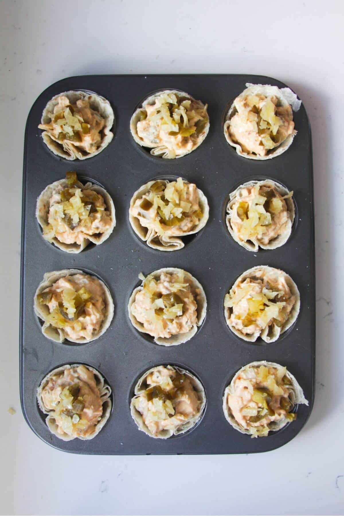 Filled jalapeno popper cups in a mini muffin tin.