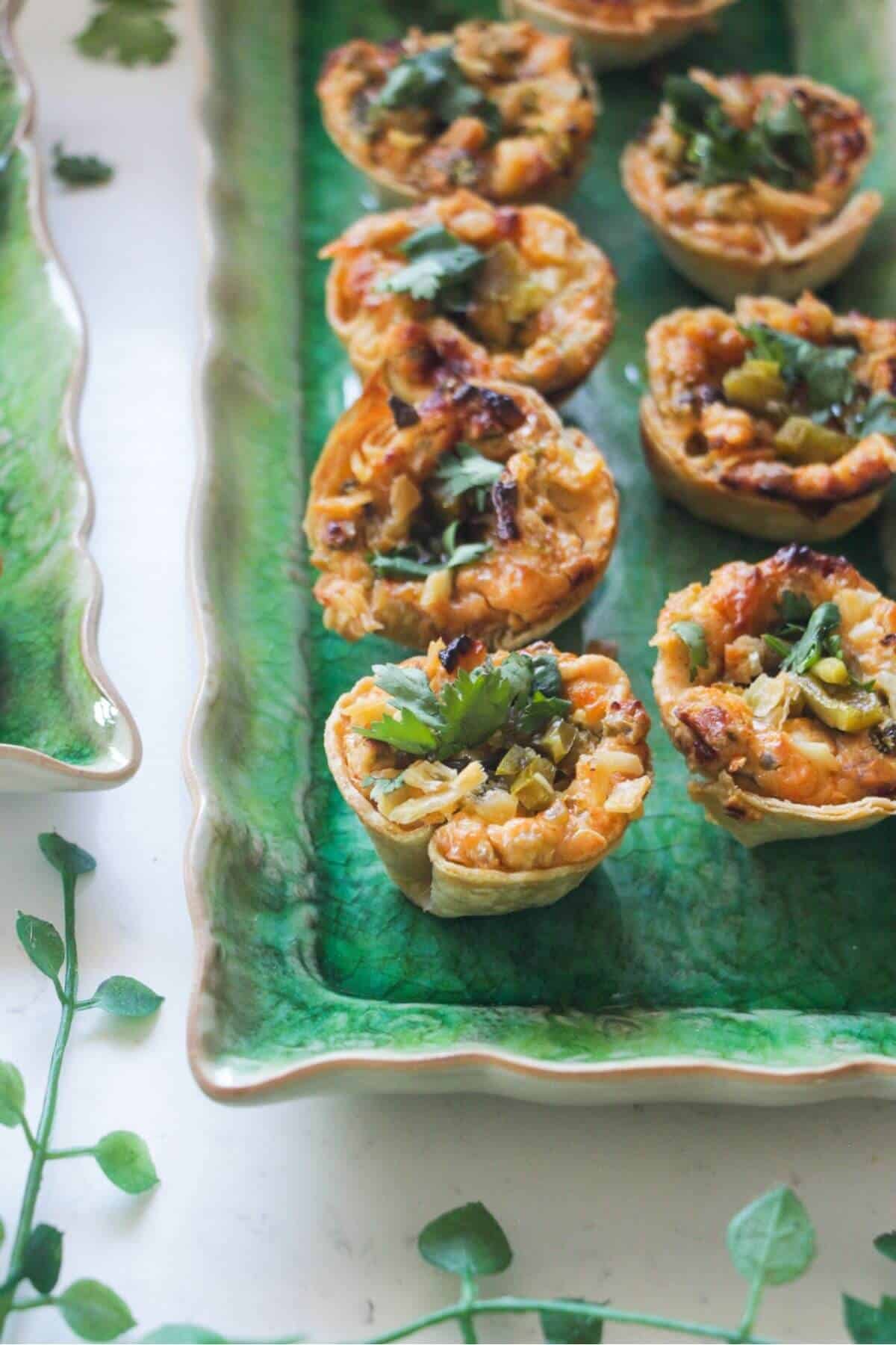 Jalapeno popper taco cups on a green rectangular plate, with a bowl of jalapenos on the side.