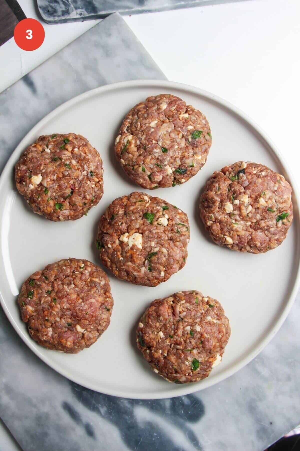 Six lamb burger patties on a large plate.