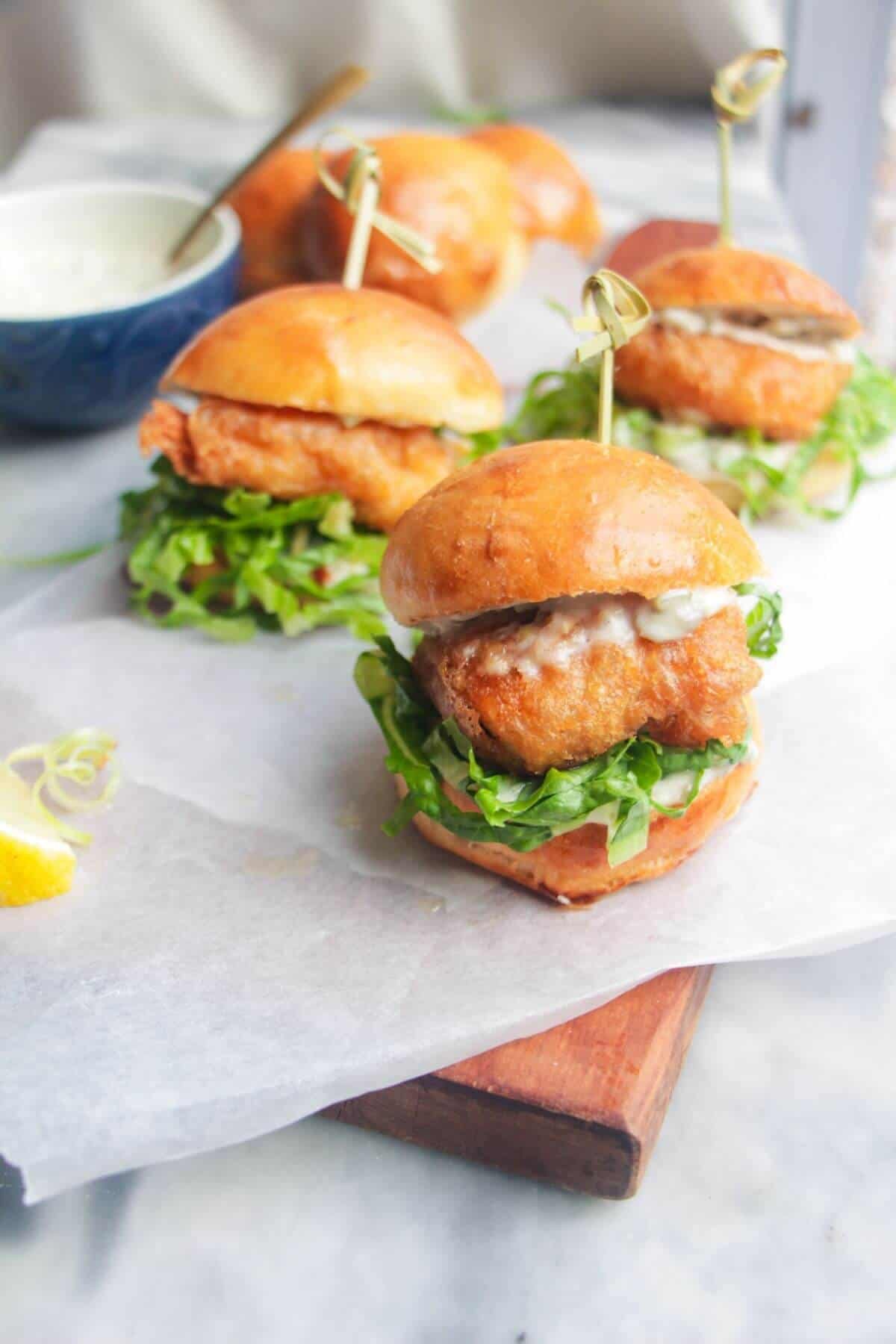 Three crispy fish sliders on a wooden board.