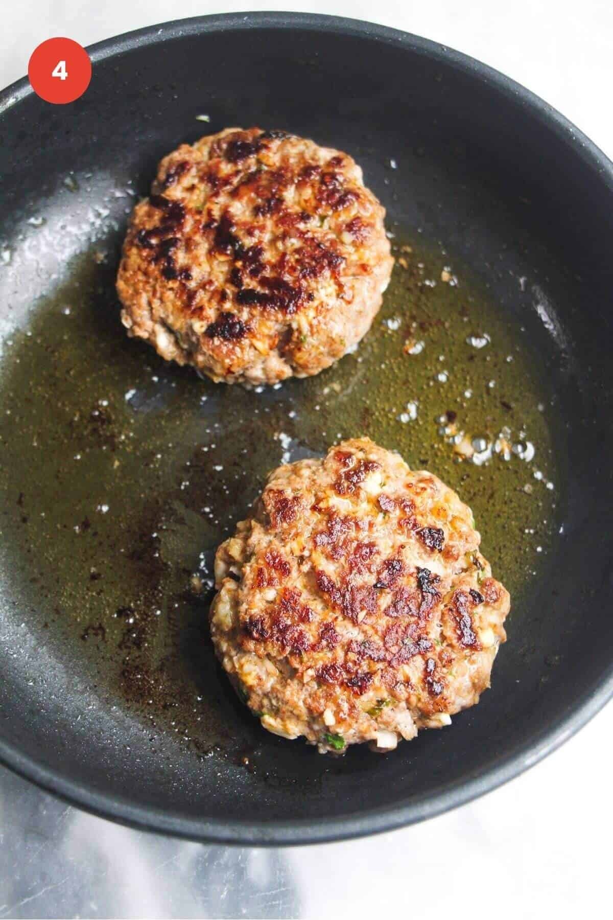 Two lamb patties cooking in a pan.