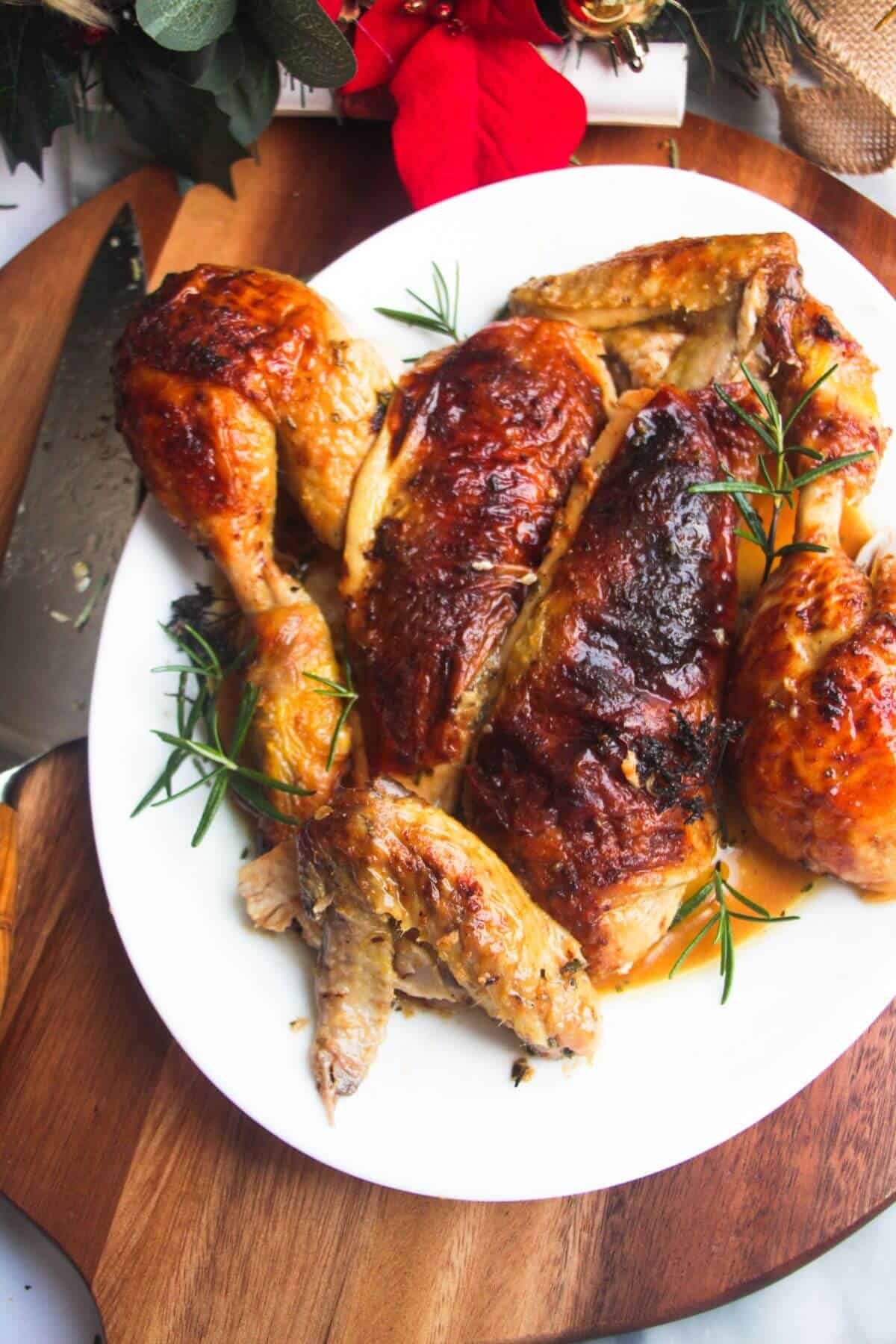 Golden carved roasted chicken on a white oval plate on a wooden board.