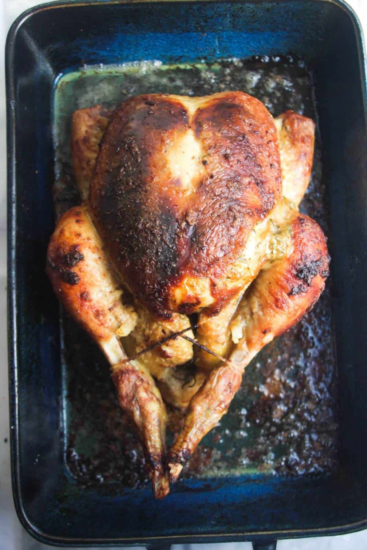 Golden brown roasted chicken after cooking, in a blue oven dish.