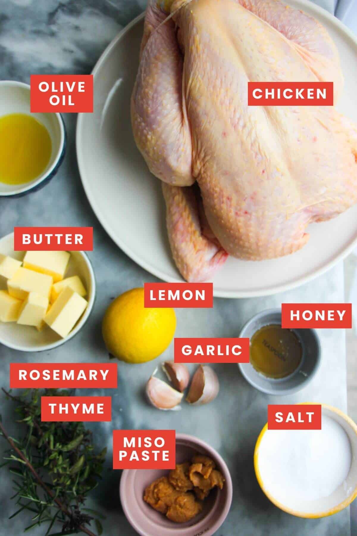 Ingredients for herb roasted chicken laid out on a grey marble background and labelled.