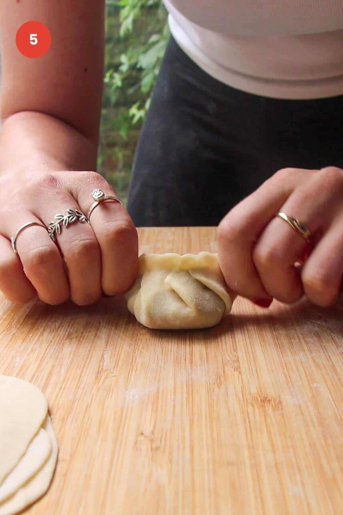 Hands sealing dumpling on wooden board.